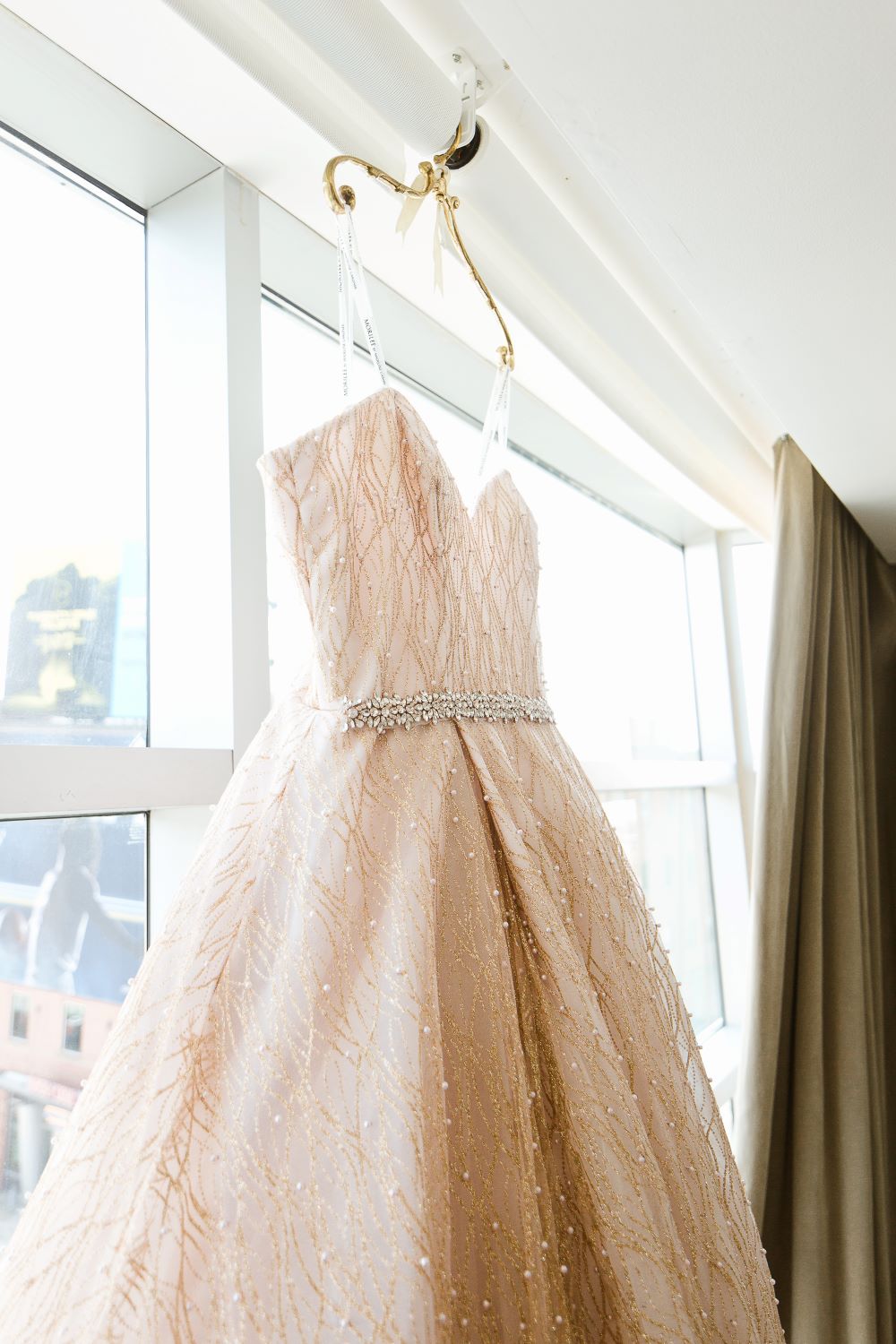 beautiful ivory and pearl beaded wedding gown hanging in a bridal suite